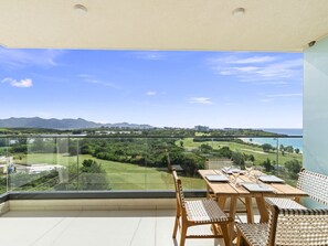 Varanda com mesa e cadeiras, vista para um campo de golfe e para o litoral.