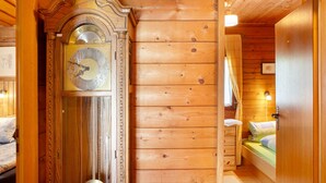A wooden interior with a large grandfather clock, a bed with a green mattress, and a wooden door. - Holiday home 'Grashäusl' with mountain views and private terrace (Grainau)