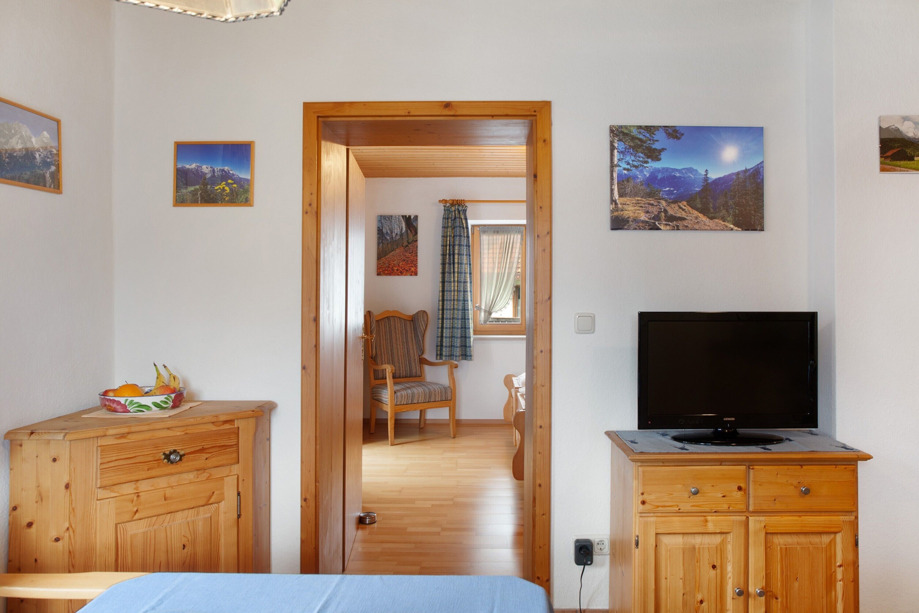 Een kamer met een bed, houten kasten, een televisie en ingelijste foto's aan de muur.