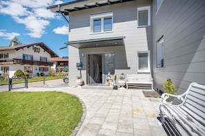 Une maison moderne à deux étages, dotée d’un porche à l’avant, d’un petit jardin et d’un banc.
