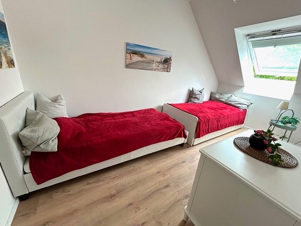 A bedroom with two beds, a window, a desk, and a plant.