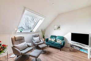 A modern living room with a sloped ceiling, a large window, a flat-screen TV, and a sofa.