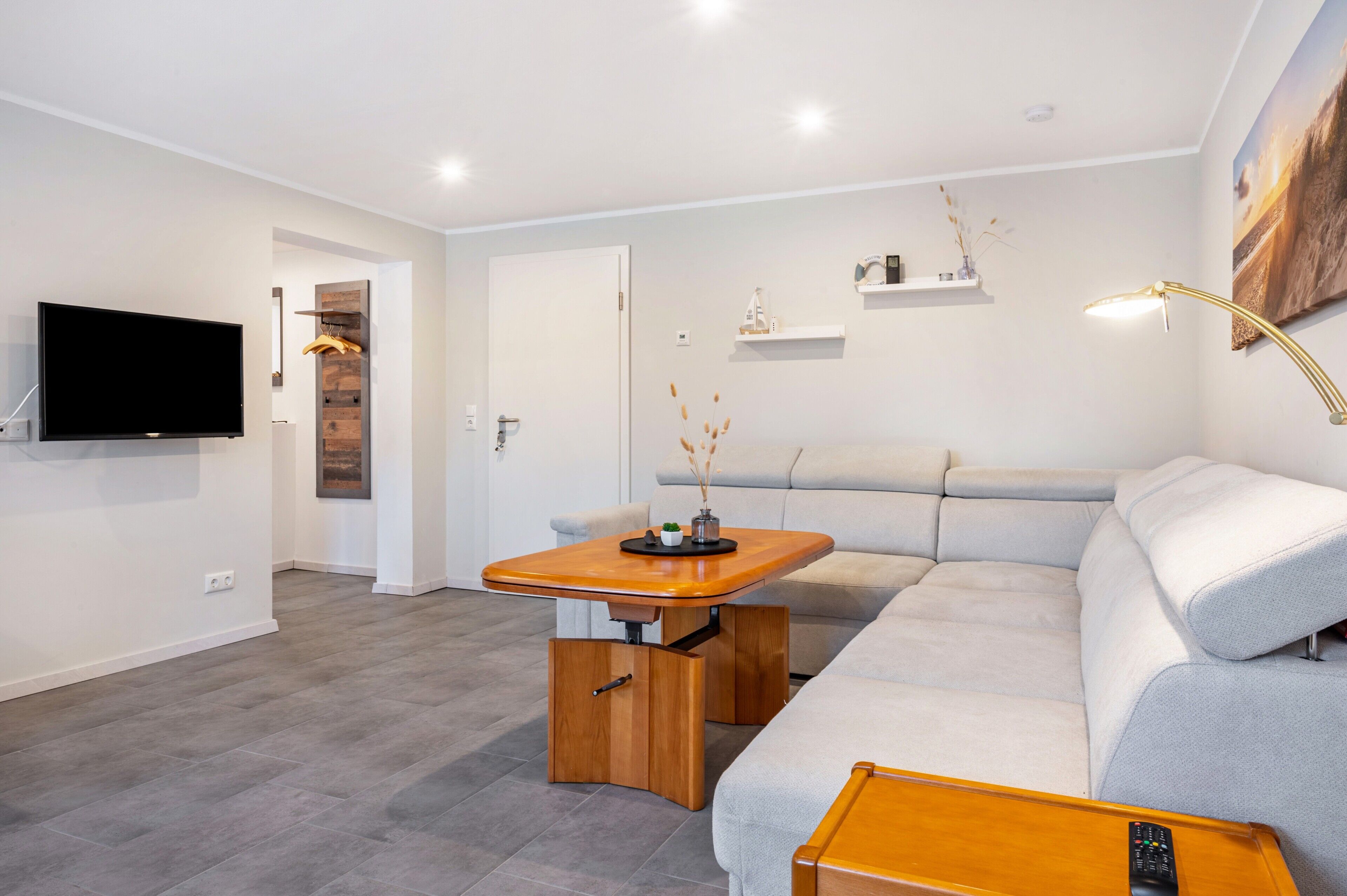 Un salon moderne avec un téléviseur à écran plat, une table basse en bois, un canapé gris et une étagère murale agrémentée d’objets décoratifs.