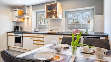 Een moderne keuken met een eetgedeelte, voorzien van een inbouwoven, een koffiezetapparaat en een eettafel gedekt met borden en een karaf.
