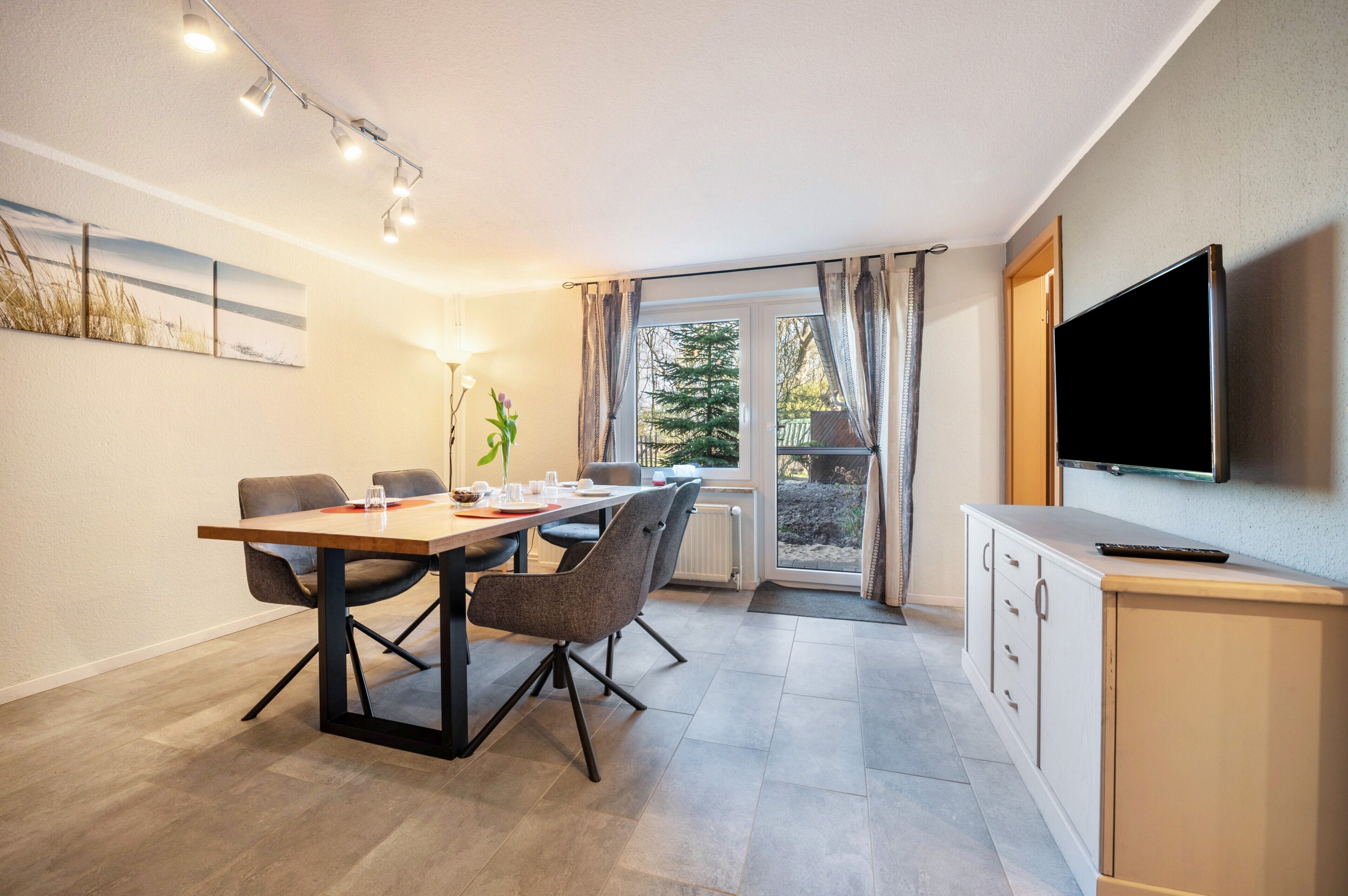 Een moderne kamer met een eettafel, stoelen, een televisie en een raam met gordijnen.