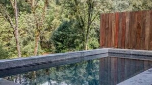 A rectangular swimming pool with a wooden fence and trees in the background. - Riverside Haven Elegant House with Serene Forest (Avandaro)