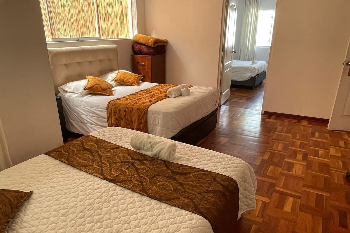 A hotel room with two beds, a wooden herringbone floor, and a window with blinds.