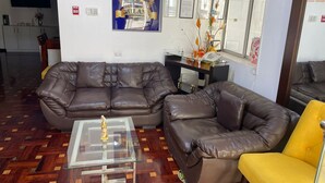 A living room with a brown leather sofa, a glass coffee table, and a yellow armchair. There are framed certificates on the wall and a fire alarm. - LIMA HOUSE MILANI (Lima)