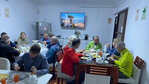 A group of people dining in a room with a television mounted on the wall, a refrigerator, and a door with a sign. - LIMA HOUSE MILANI (Lima)
