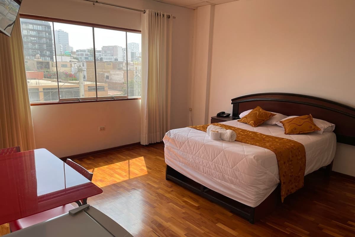 A hotel room with a bed, a desk, and a window with a city view.