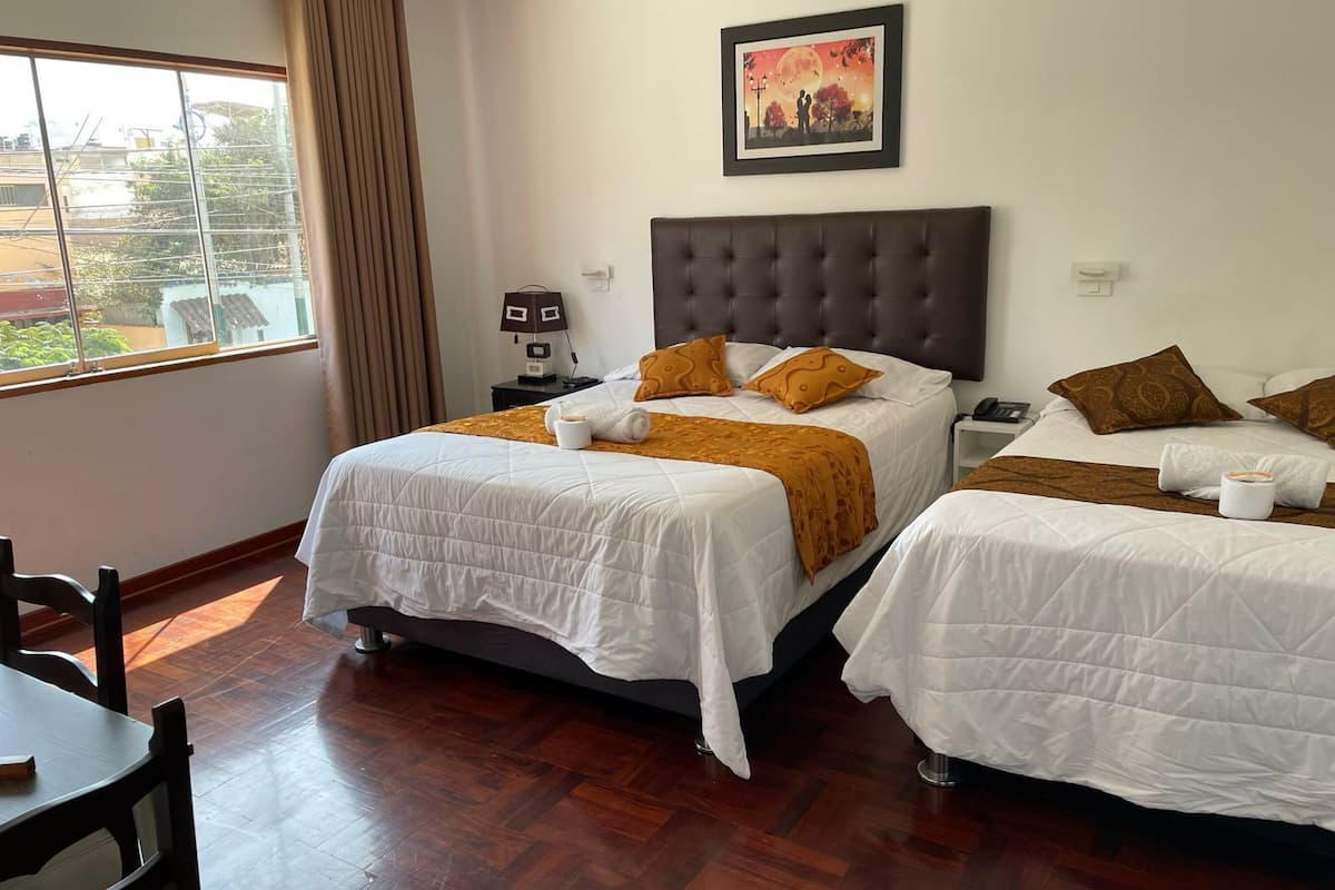 A hotel room with two beds, a large window, a painting, and a small table.