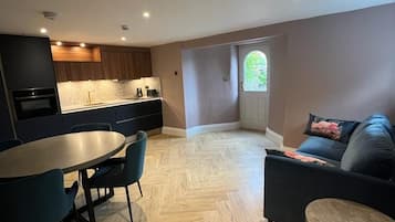 A modern kitchen with dark cabinetry, a dining table with chairs, and a living area with a sofa and a small round table.