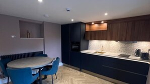 Una cocina moderna con armarios oscuros, piso de madera en patrón de espiga y una mesa redonda con sillas azules.