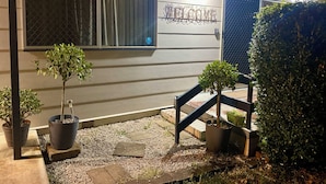 A house with a 'WELCOME' sign, potted plants, and a gravel pathway.