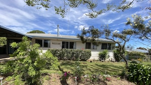 A house with a "WELCOME" sign, surrounded by a well-maintained garden with various plants and a clear blue sky.