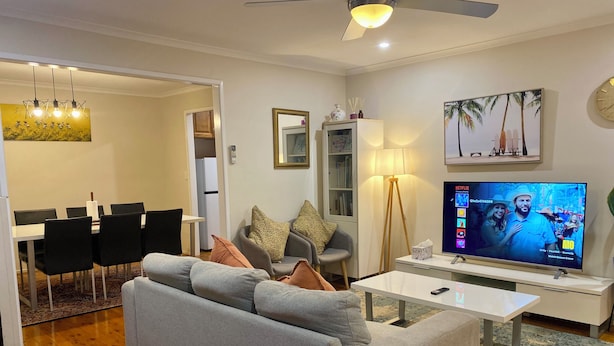 A modern living room with a grey sofa, a dining table with chairs, a TV, and a ceiling fan.