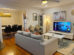 A modern living room with a grey sofa, a dining table with chairs, a TV, and a ceiling fan.