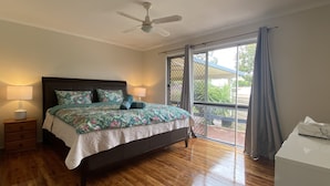 A bedroom with a bed, two bedside tables with lamps, a ceiling fan, and a view through a sliding glass door to an outdoor area.