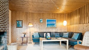 Ett mysigt vardagsrum med ett träpanelat tak, en tegelkamin, en soffgrupp, ett soffbord och en hängande lampa.
