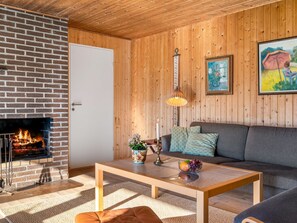 Ein gemütliches Wohnzimmer mit Kamin aus Backsteinen, Holzwänden, einer Couch, einem Couchtisch und einer Hängelampe.