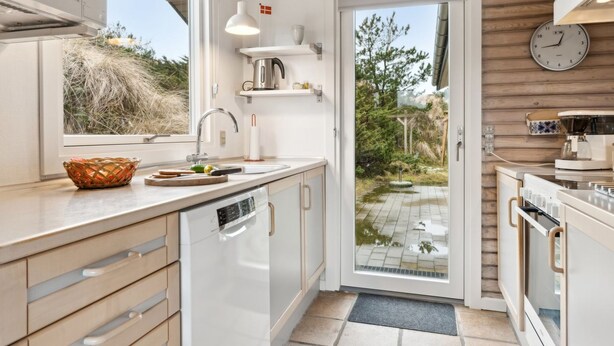 Una cocina moderna con armarios blancos, lavavajillas integrado, pileta de acero inoxidable y cafetera.