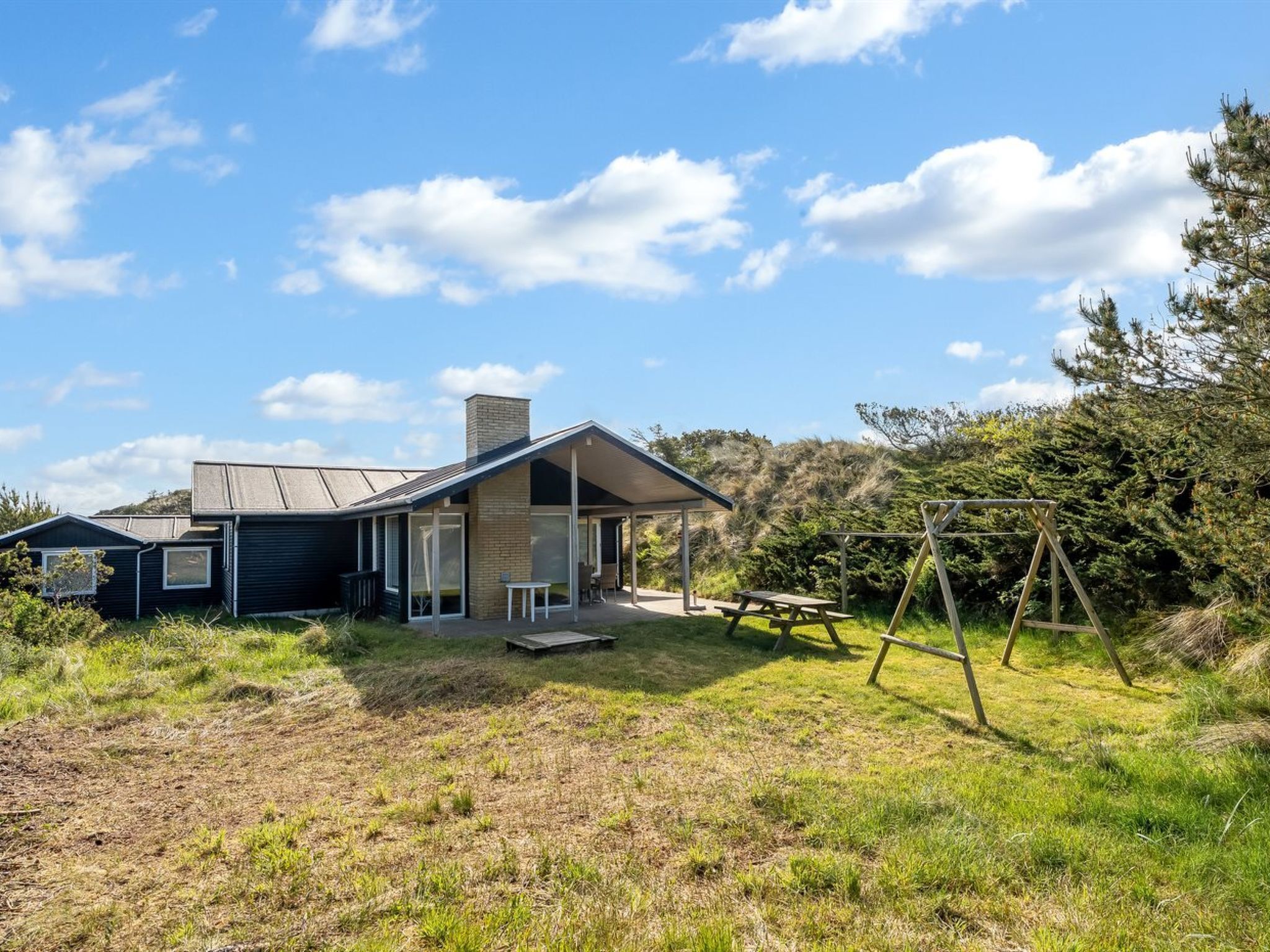 A modern house with a large patio, a swing set, and a grassy yard.