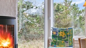 Una habitación con chimenea, vista a árboles y cielo despejado, y una silla estampada.