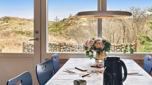 Un comedor con una mesa dispuesta para dos, un jarrón de flores y vistas a un paisaje natural a través de amplios ventanales.