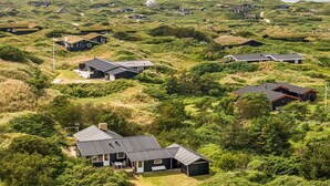 Zona residencial costera con casas construidas sobre dunas cubiertas de hierba, que presenta arquitectura moderna y cercanía al mar.