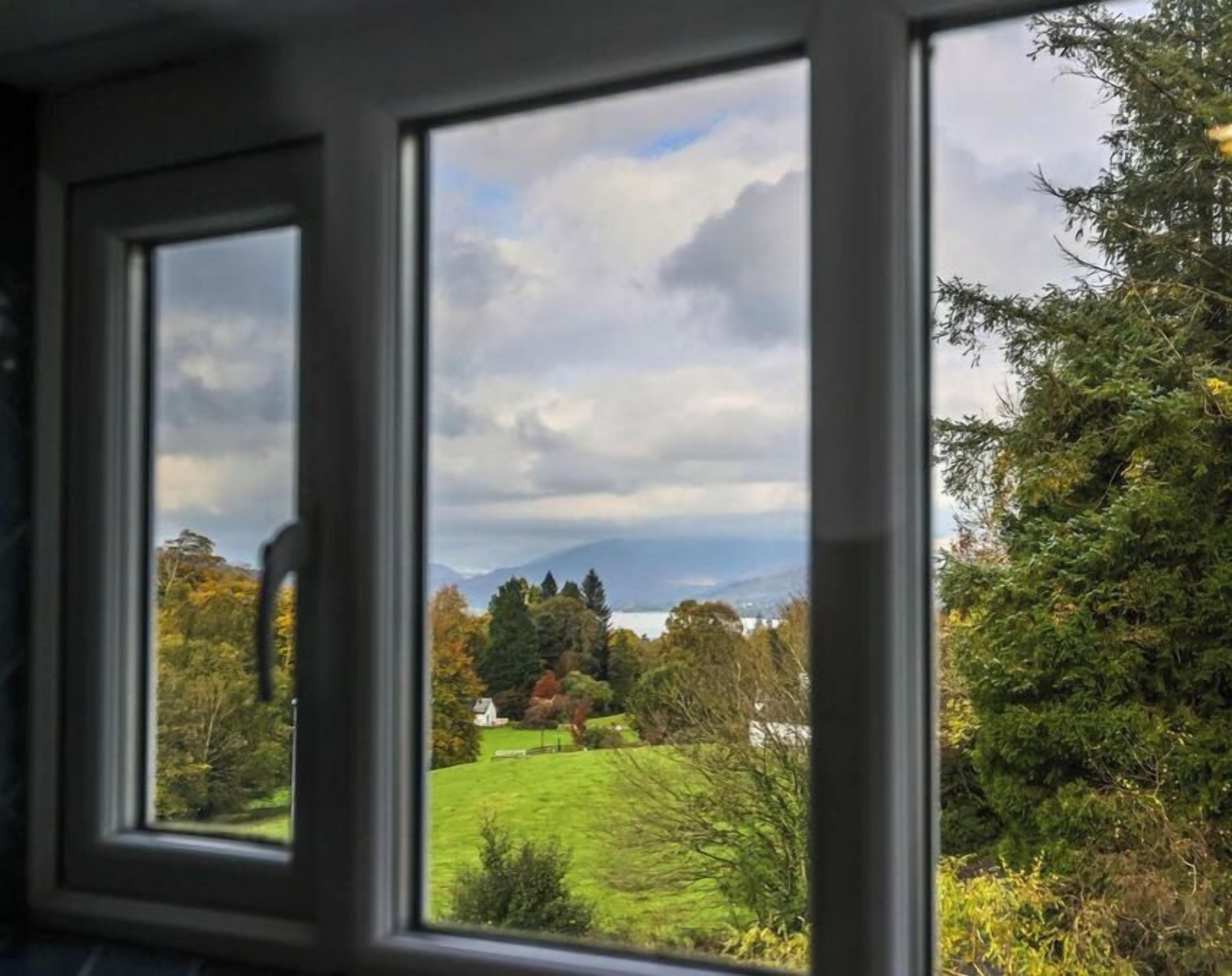 Ein Fenster mit Blick auf eine grüne Landschaft, Bäume und ein Haus.
