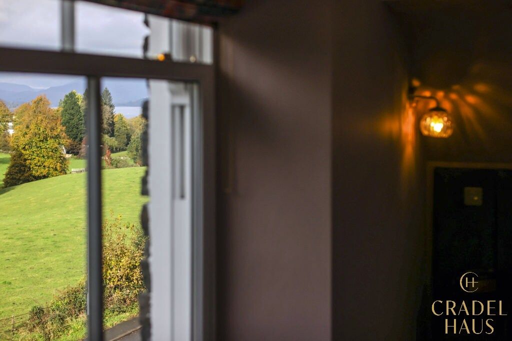 Una habitación con ventana que da a un paisaje verde, una puerta y una lámpara fijada a la pared.