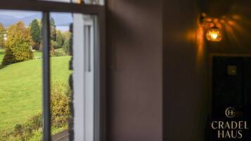 Una habitación con ventana que da a un paisaje verde, una puerta y una lámpara fijada a la pared.
