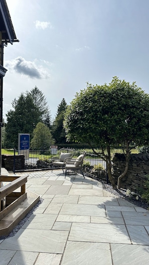 An outdoor patio area with stone flooring, a wooden bench, and a metal fence. - Luxe Duplex with EV Charger & Pet-Friendly (Bowness-on-Windermere)
