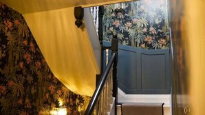Un escalier orné d’un papier peint à motifs floraux, un mur bleu foncé et un luminaire placé sur le côté gauche.