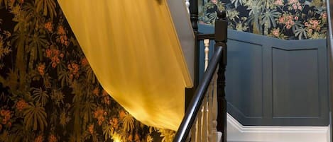 Step into elegance at Windermere with a gorgeous hallway and stairs adorned with luxury floral print wallpaper and edged carpet runners, setting the tone for a truly sophisticated and welcoming retreat.