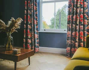 Relax in style at Windermere with a view – a picture-perfect coffee table graces the living room alongside a second sofa, positioned by the large window offering glorious views of Lake District greenery. Perfect for unwinding in serenity. - Luxe Duplex with EV Charger & Pet-Friendly (Bowness-on-Windermere)