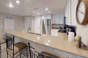 Enjoy cooking in this well-equipped kitchen with a central island, sink, and refrigerator, perfect for preparing meals before heading out to the beach.