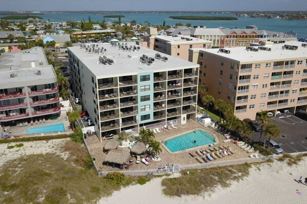 A multi-story hotel with a rooftop pool, a smaller pool, and a beach area with lounge chairs.