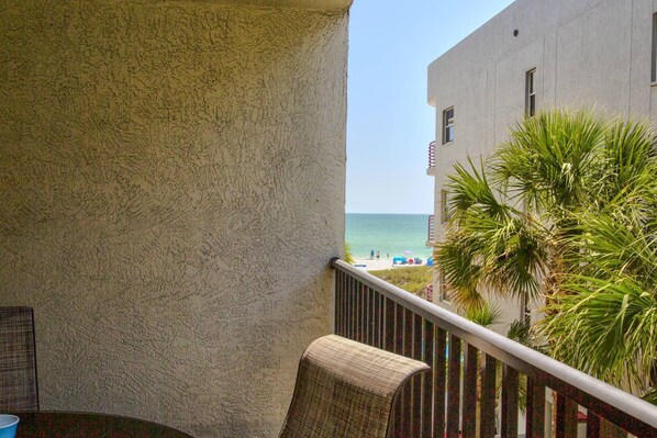 A balcony with a view of the beach and palm trees. - Sandy Toes & Starlit Nights! Heated Pool, Beach, Shopping, Restaurants. Beachfront Resort. (Madeira Beach)