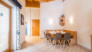 A dining area with a wooden table and chairs, a wooden ceiling, and a tiled floor.