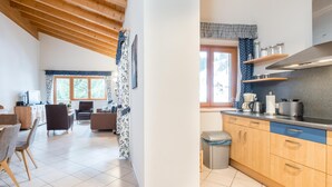 A spacious living area with a high wooden ceiling, a kitchen with modern appliances, and a dining area with a table and chairs.