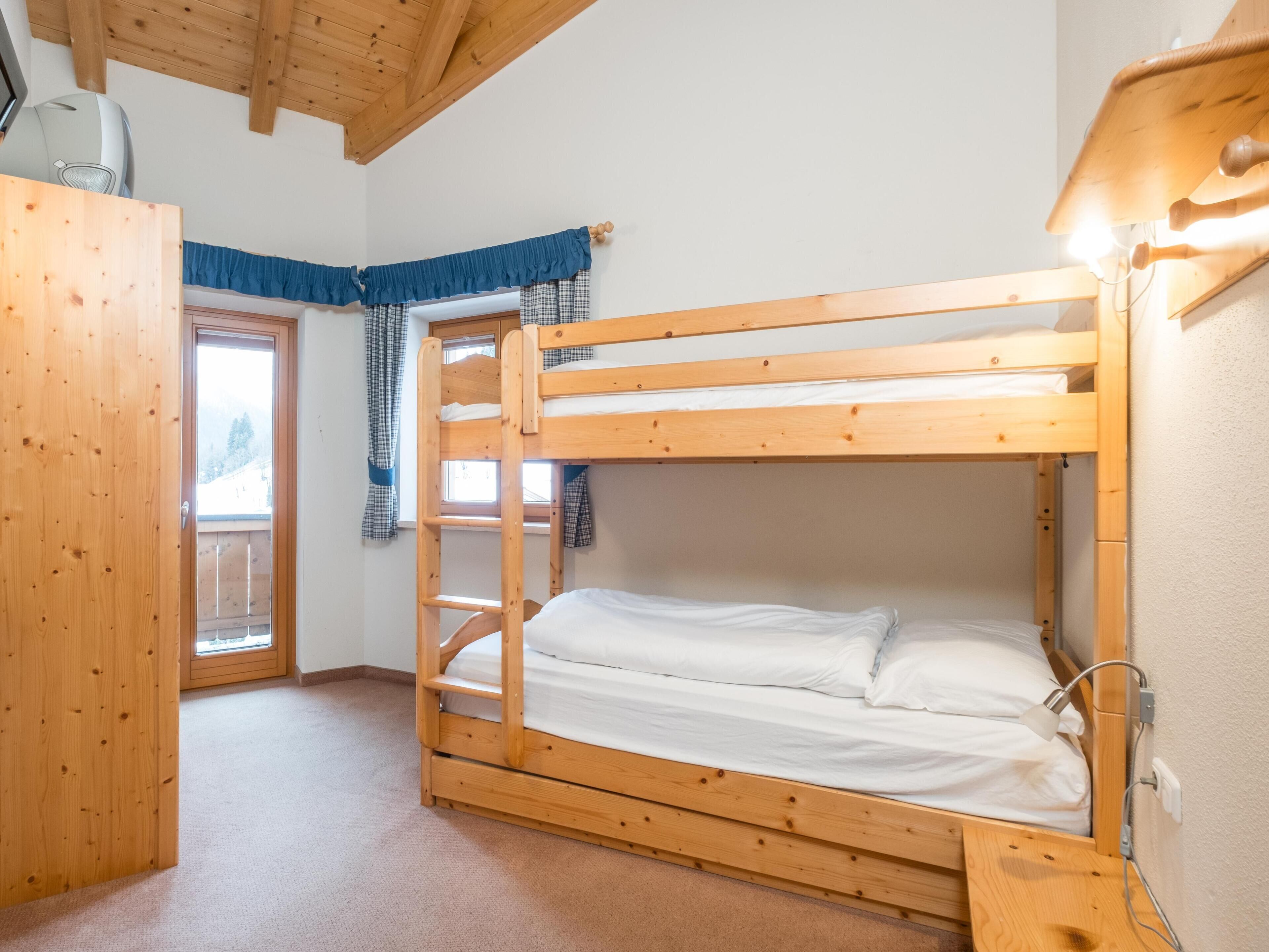 Habitación con literas, techo de madera, ventana con cortinas y una puerta.