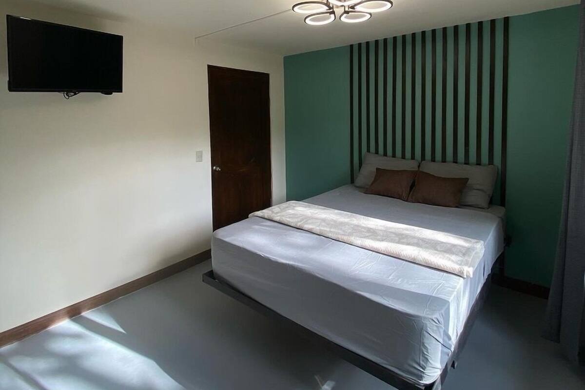 A bedroom with a bed, a TV mounted on the wall, and a unique ceiling light fixture.