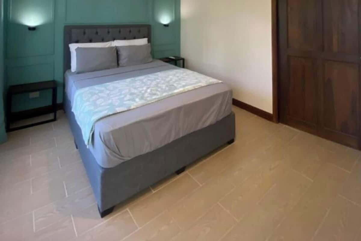 A bedroom with a bed, two bedside tables, a hanging light fixture, and a wooden door.