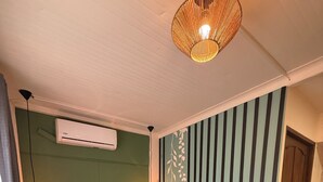 A bedroom with a large bed, a wall-mounted air conditioner, a hanging light fixture, and a striped wall decoration. - Oasis by Franklin Hotel Boutique (La Fortuna)