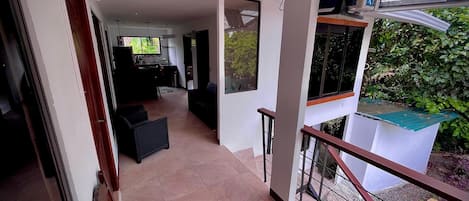 Un vaste espace de vie comprenant une cuisine, un balcon avec vue sur la verdure et un escalier menant à l’étage supérieur.