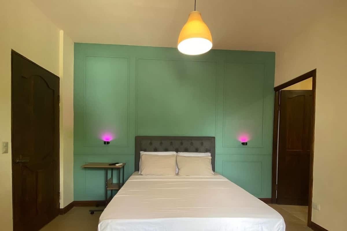 A bedroom with a bed, two bedside lamps, a nightstand, and a hanging light fixture.