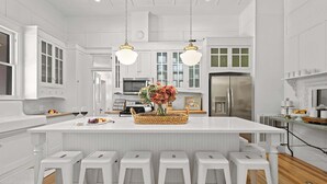 A modern kitchen with white cabinetry, a central island with stools, and a hanging light fixture.