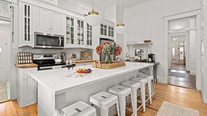 A kitchen with white cabinetry, a large island with stools, a microwave, and a hanging light fixture.