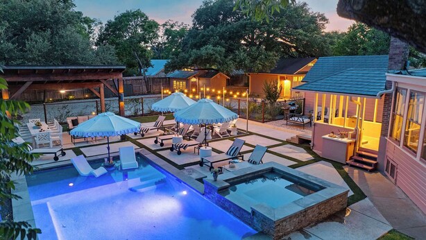 A backyard with a swimming pool, lounge chairs, umbrellas, and a barbecue area.